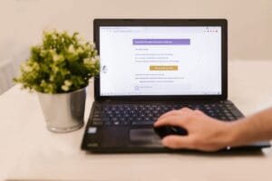 Pessoa lendo um e-mail no notebook, sobre uma mesa com um vaso de planta